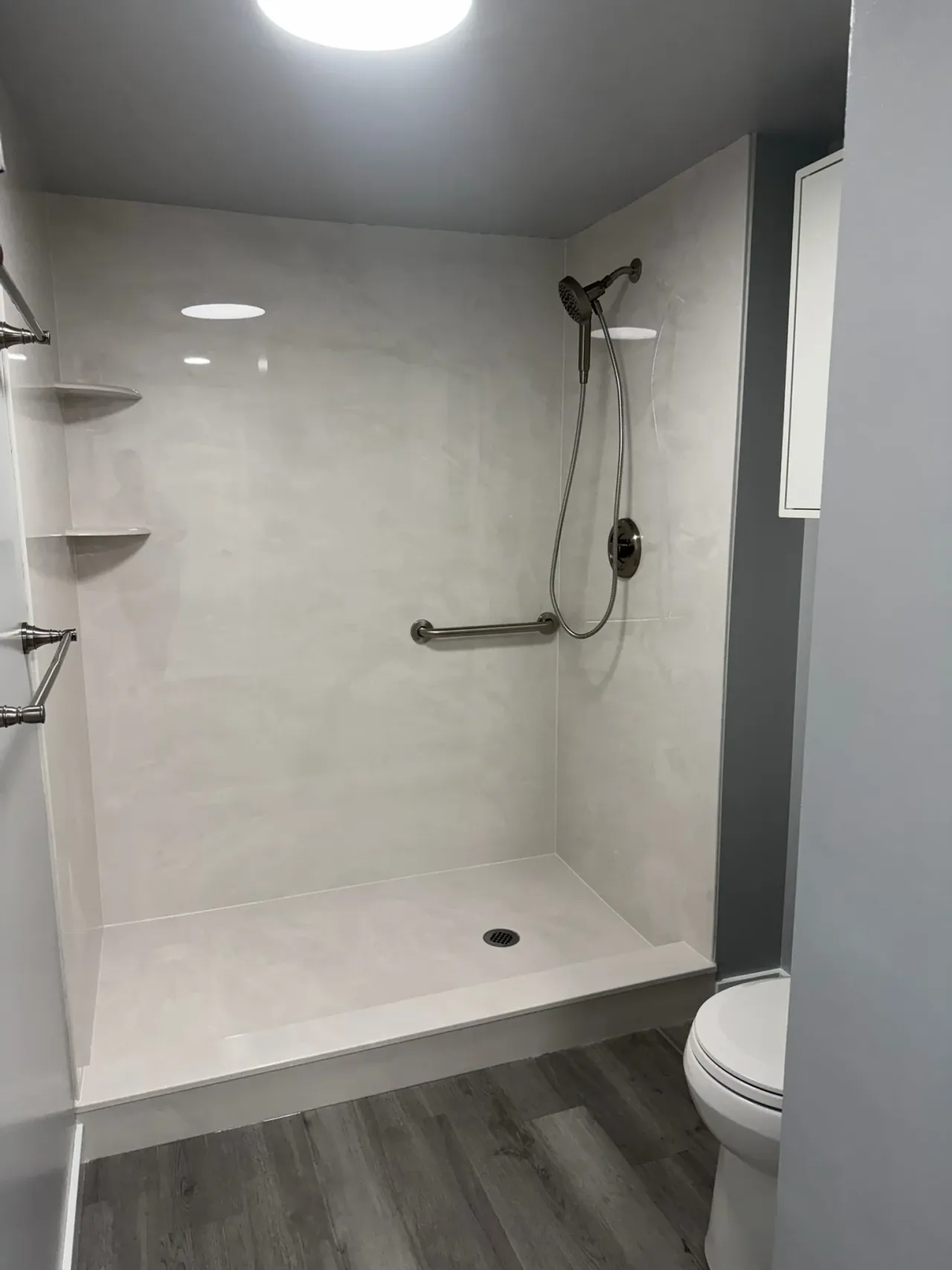 Walk-in shower with marble-look wall panels, handheld showerhead, and grab bar