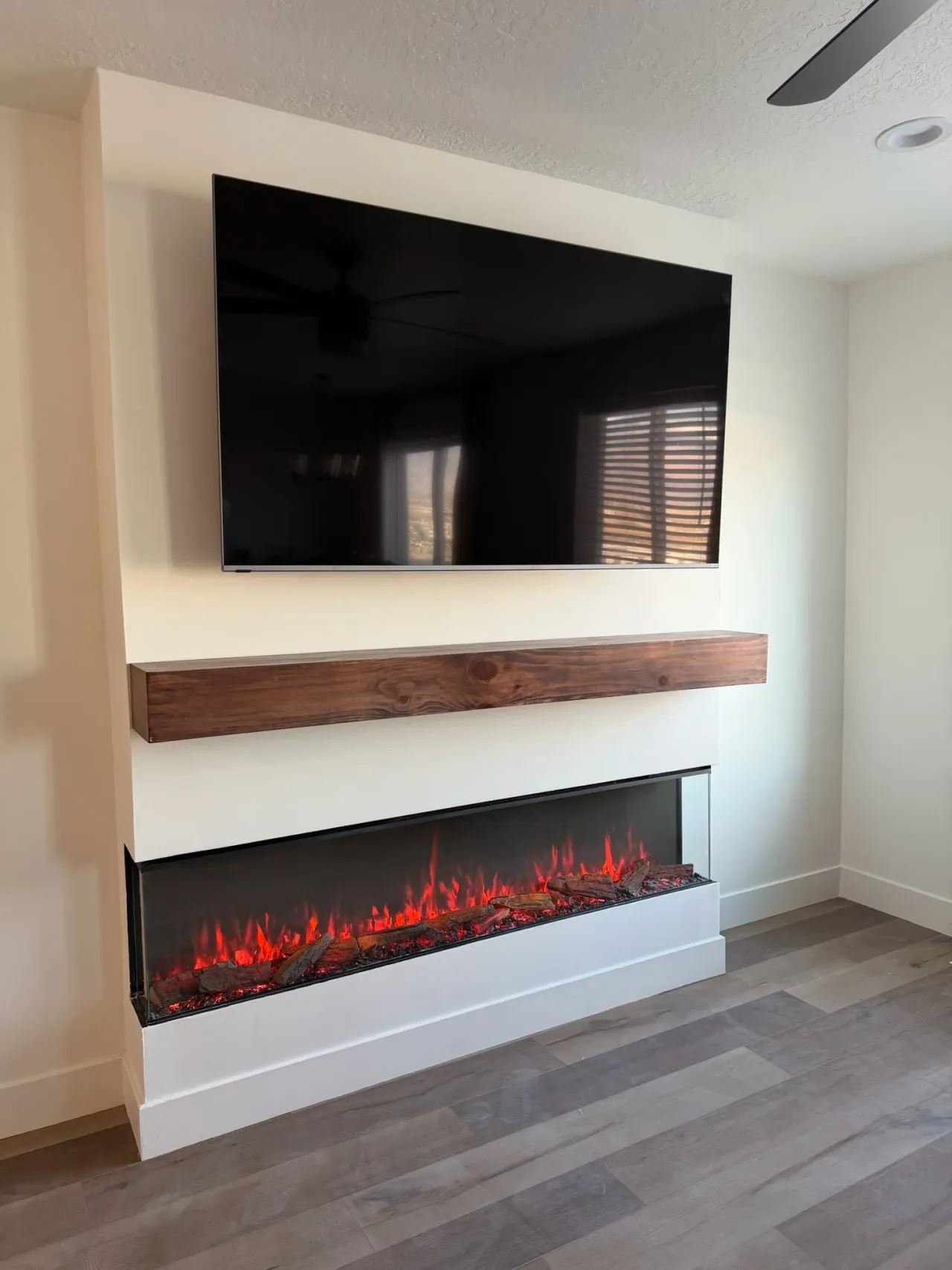 Modern electric corner fireplace with floating wood mantel and wall-mounted TV