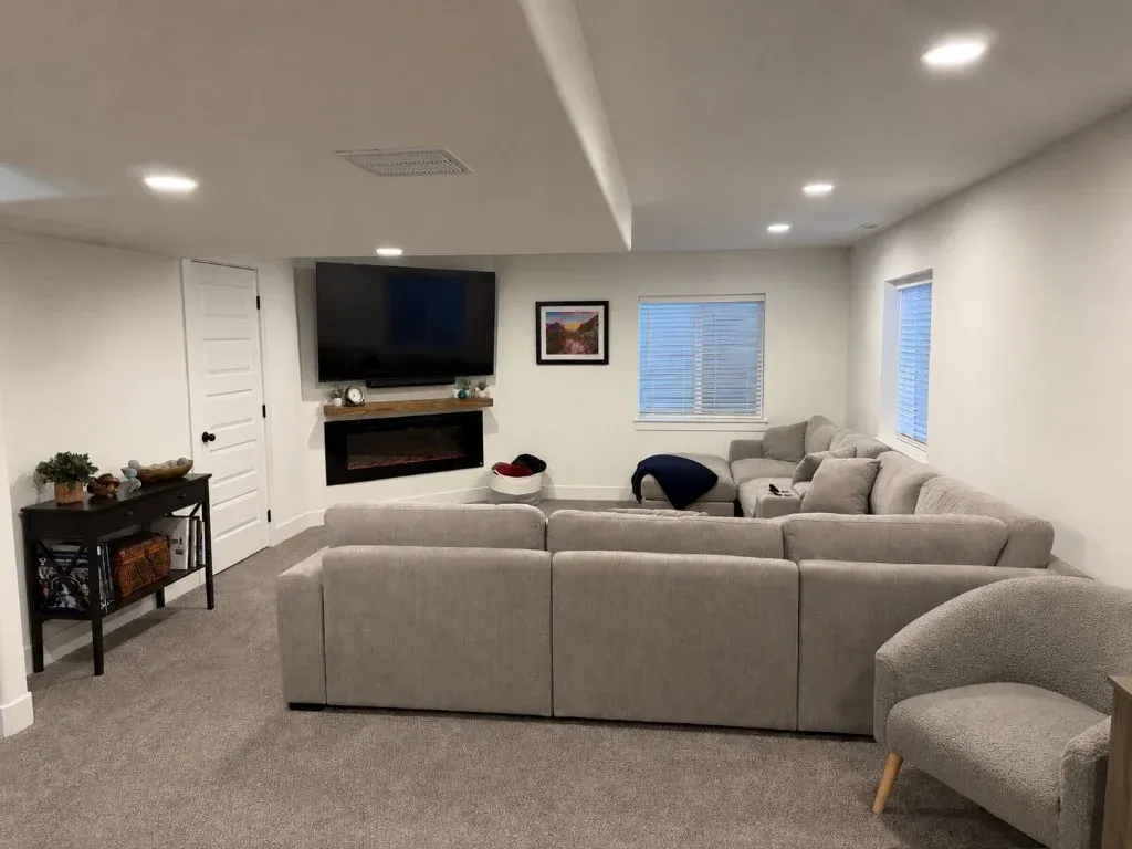 Finished basement living space with sectional sofa, wall-mounted TV, and electric fireplace in a Utah home